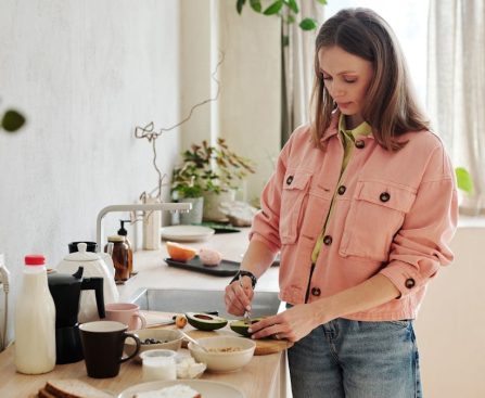 A woman slices an avocado in a bright, modern kitchen with natural light.