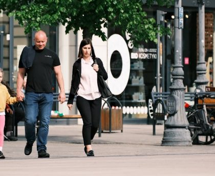 A family walks past storefronts and bicycles in a lively shopping district.