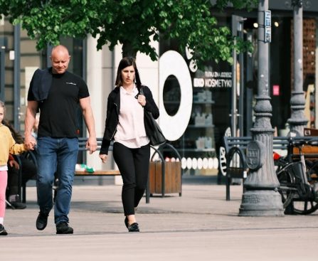 A family walks past storefronts and bicycles in a lively shopping district.