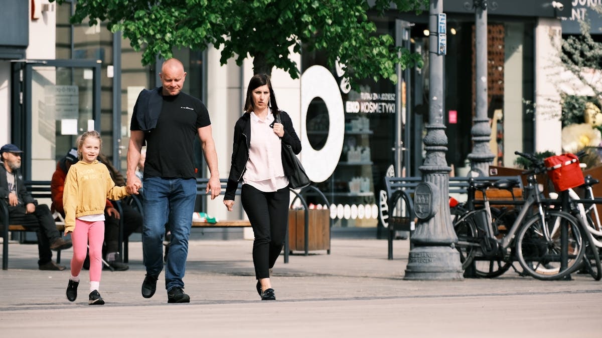 A family walks past storefronts and bicycles in a lively shopping district.